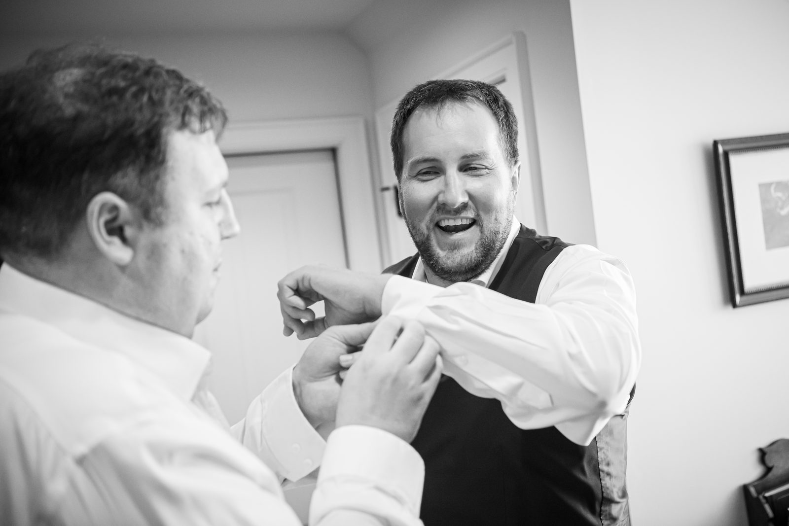 A groomsman fastening a cufflink, both of them laughing
