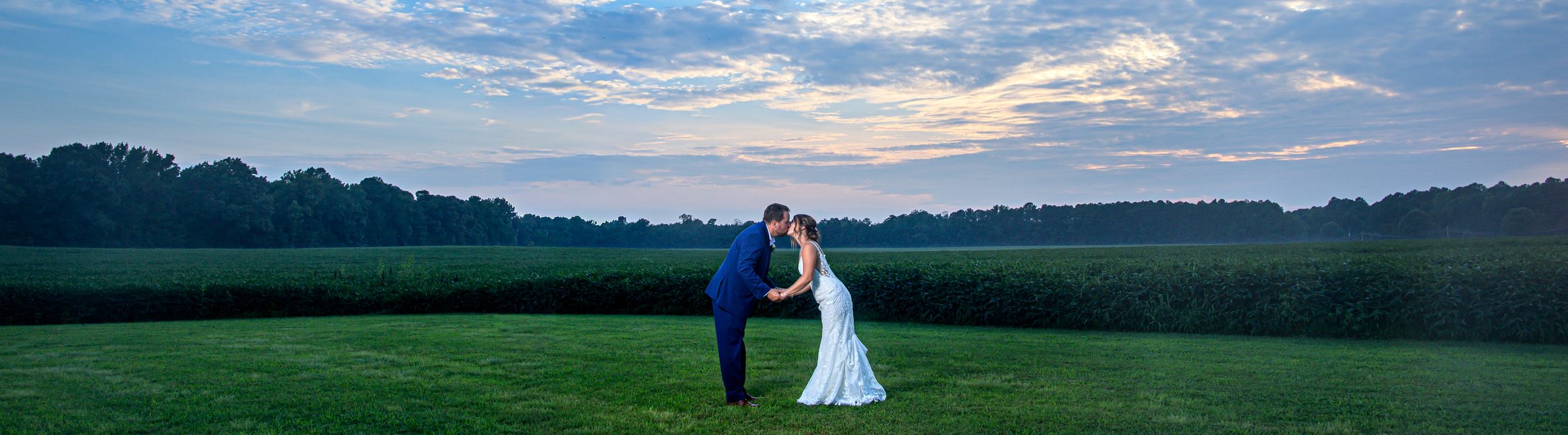 Maria and Jeremy kissing in a wide green field at dusk